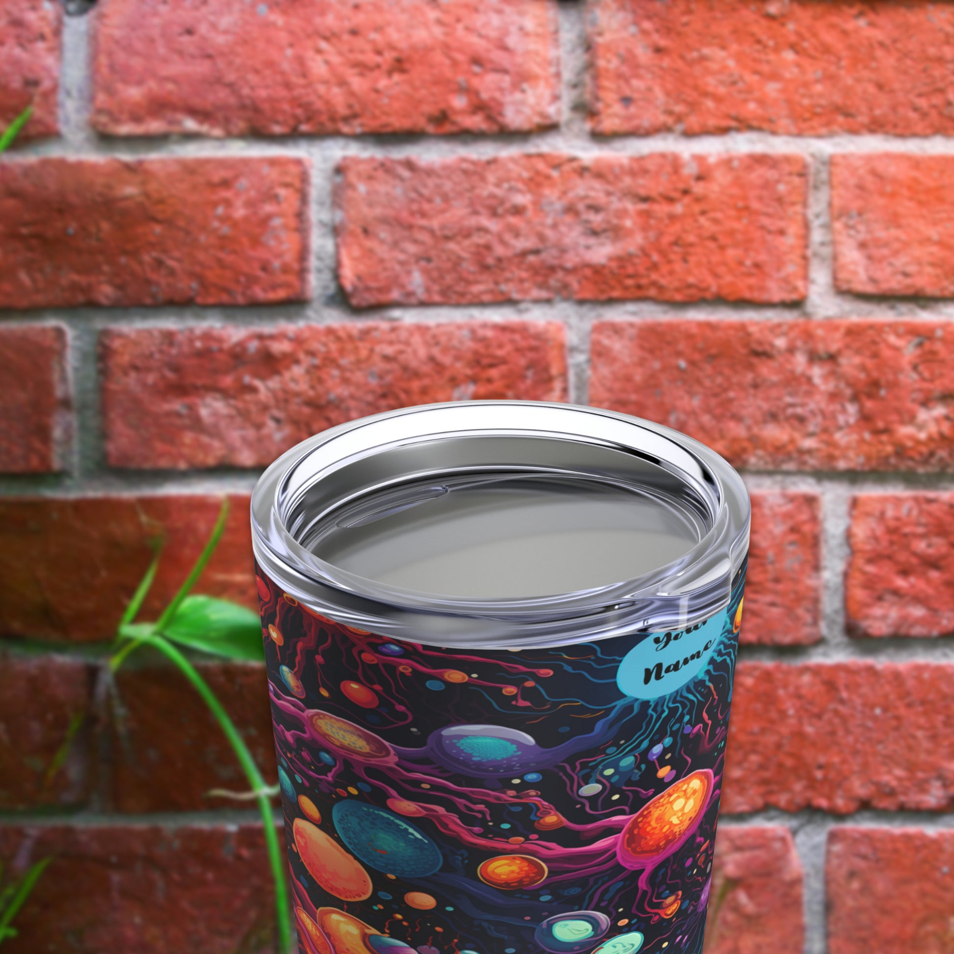 Biology-themed tumbler with cosmic design featuring planets and stars, ideal for science lovers. Vibrant, colorful tumbler placed on a wooden surface with greenery and a brick wall in the background, perfect for students and biology enthusiasts